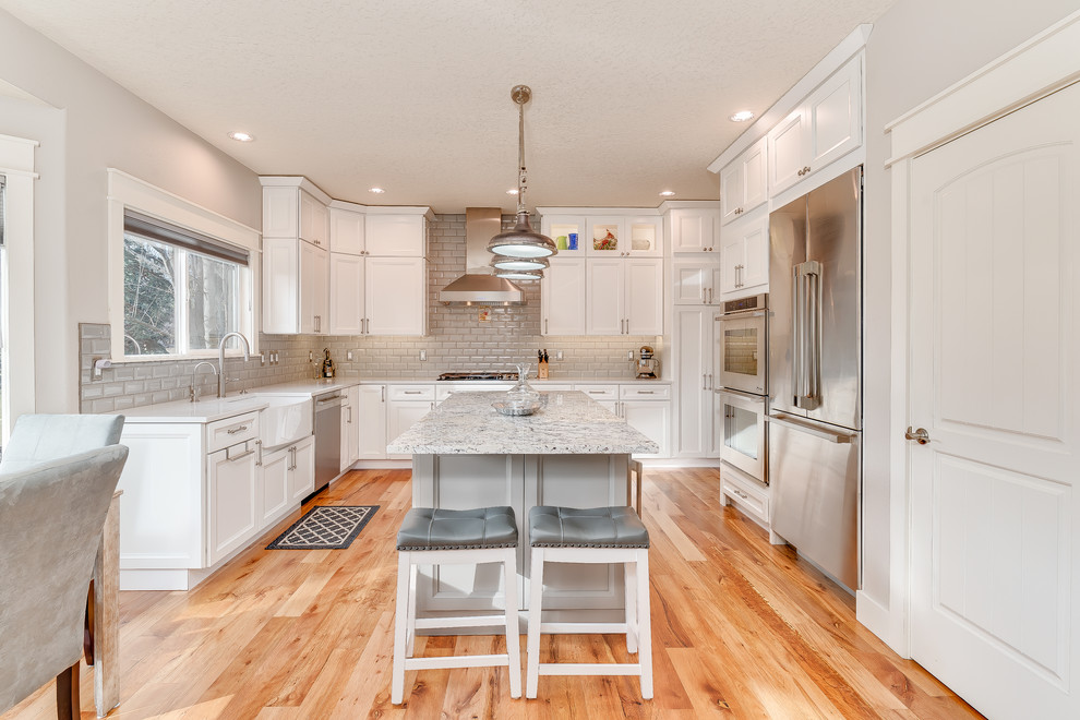 Example of a mid-sized transitional u-shaped medium tone wood floor and brown floor eat-in kitchen design in Boise with a farmhouse sink, shaker cabinets, white cabinets, quartz countertops, gray backsplash, subway tile backsplash, stainless steel appliances and an island