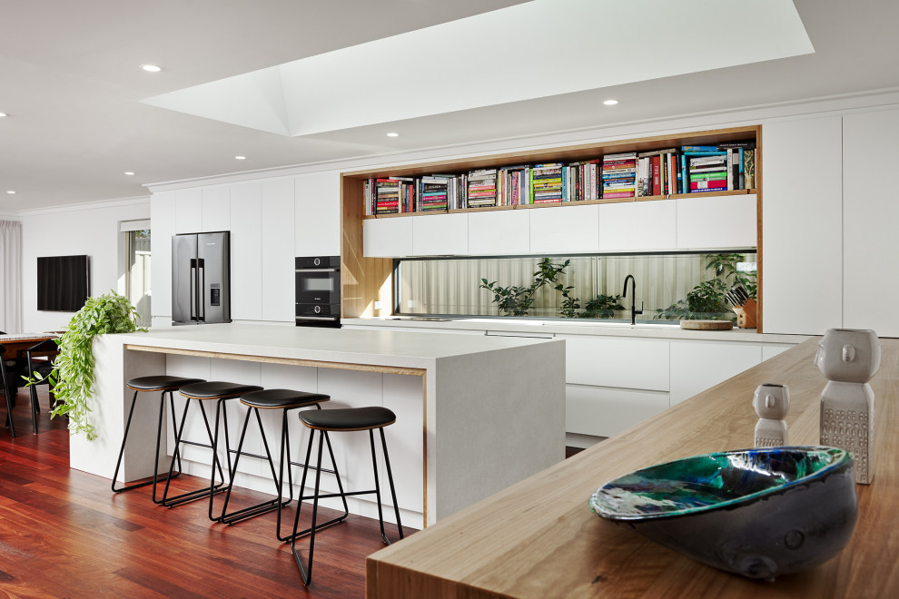 Design ideas for a large contemporary l-shaped eat-in kitchen in Perth with an undermount sink, flat-panel cabinets, white cabinets, quartz benchtops, window splashback, black appliances, dark hardwood floors, with island, brown floor and white benchtop.