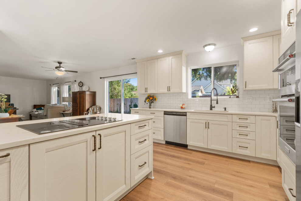Design ideas for a medium sized contemporary kitchen/diner in Seattle with a double-bowl sink, shaker cabinets, white cabinets, engineered stone countertops, white splashback, porcelain splashback, stainless steel appliances, laminate floors, a breakfast bar, brown floors and white worktops.