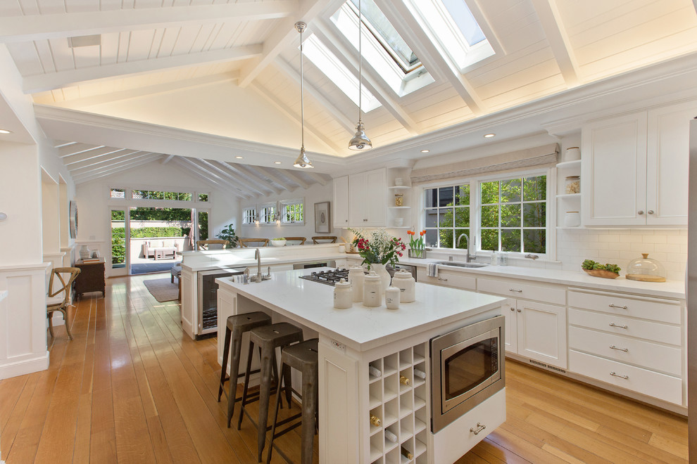 Inspiration for a transitional l-shaped medium tone wood floor and brown floor kitchen remodel in San Francisco with an undermount sink, white backsplash, subway tile backsplash, stainless steel appliances and white countertops