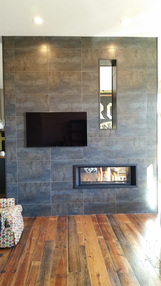 Photo of a mid-sized transitional loft-style living room in Milwaukee with white walls, medium hardwood floors, a two-sided fireplace, a tile fireplace surround and a wall-mounted tv.