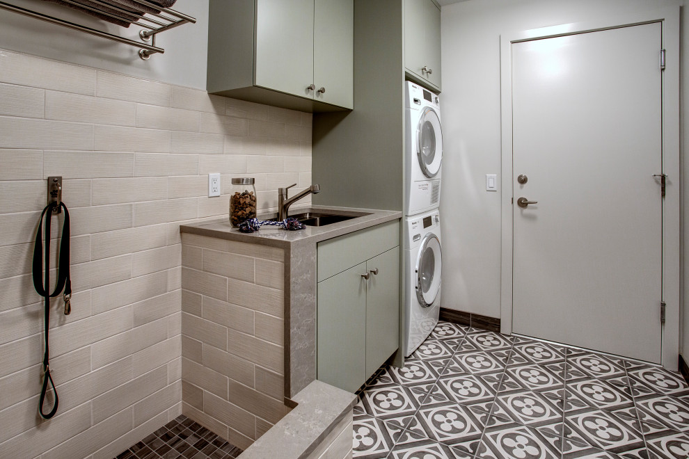 Transitional laundry room in Seattle with an utility sink, flat-panel cabinets, green cabinets, quartz benchtops, white splashback, ceramic splashback, white walls, porcelain floors, a stacked washer and dryer, multi-coloured floor and grey benchtop.