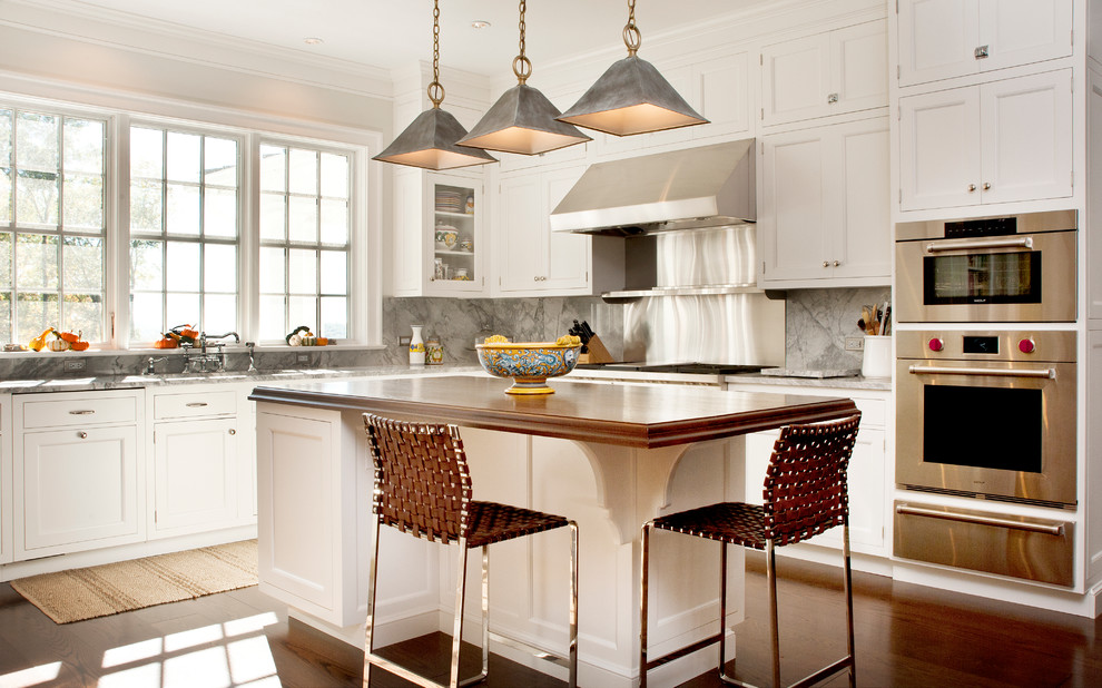 Example of a country u-shaped dark wood floor kitchen design in New York with an undermount sink, recessed-panel cabinets, white cabinets, marble countertops, gray backsplash, stainless steel appliances and an island