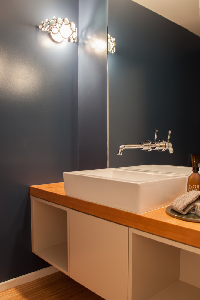 This is an example of a midcentury powder room in Los Angeles with a vessel sink, flat-panel cabinets, wood benchtops, light hardwood floors, white cabinets and brown benchtops.