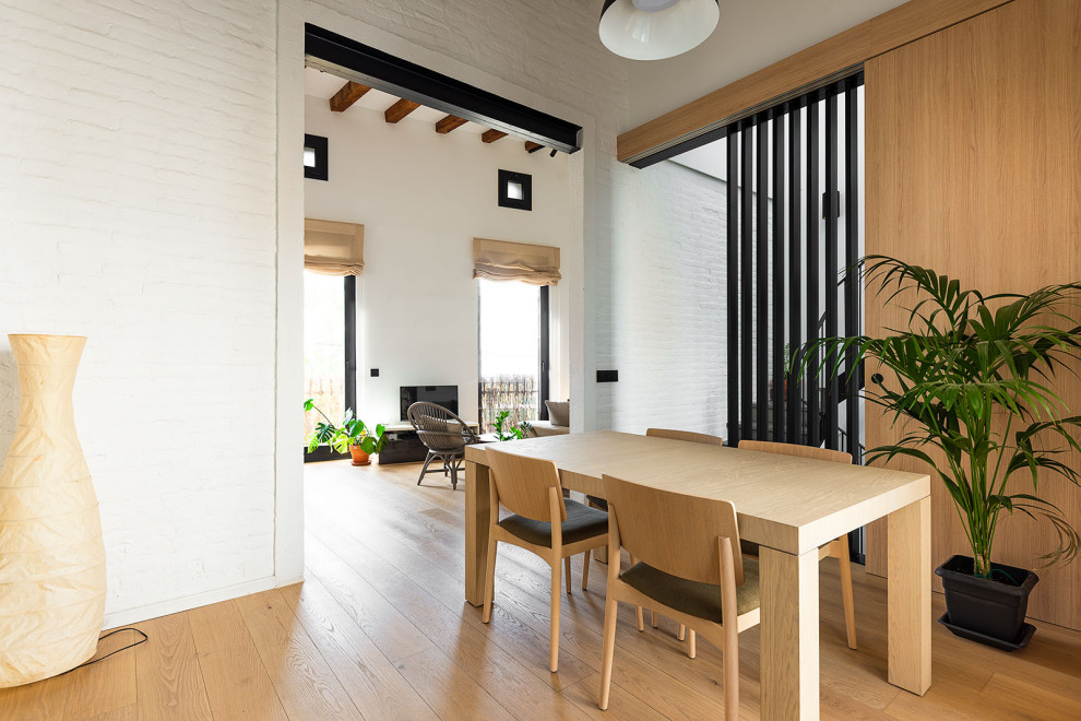 Mid-sized scandinavian open plan dining in Barcelona with white walls, light hardwood floors and exposed beam.