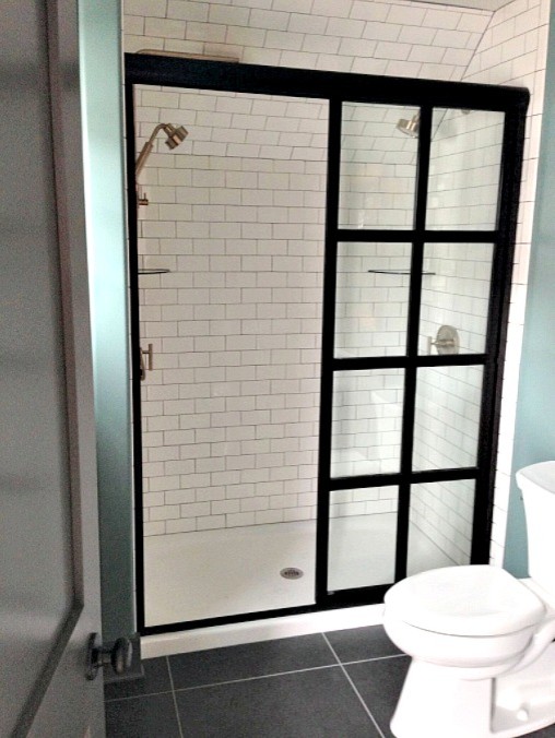 Photo of a mid-sized industrial 3/4 bathroom in Other with open cabinets, yellow cabinets, an alcove shower, a two-piece toilet, gray tile, white tile, subway tile, green walls, ceramic floors and a console sink.