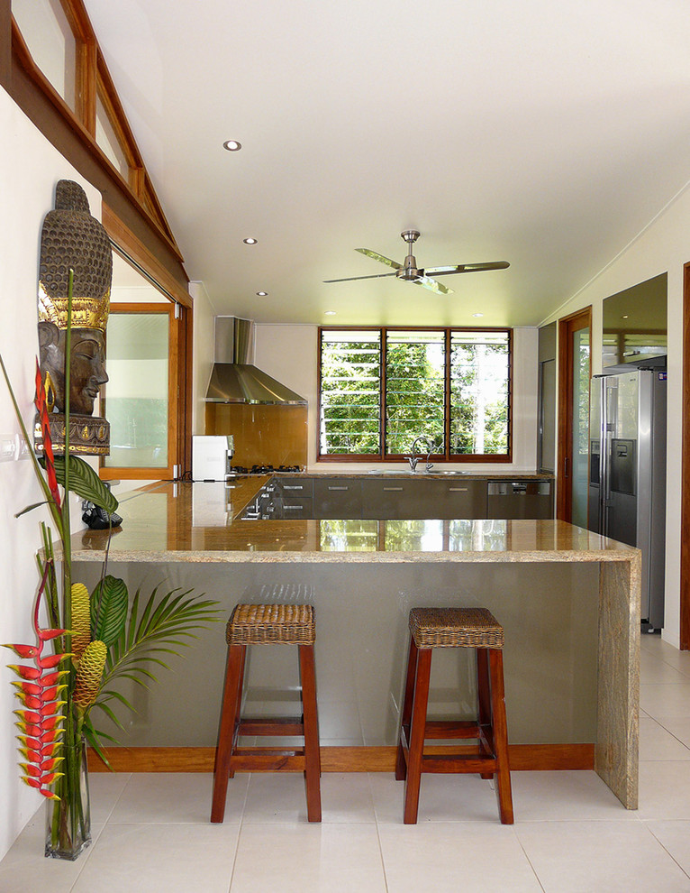 Mid-sized tropical u-shaped eat-in kitchen in Brisbane with flat-panel cabinets, granite benchtops, stainless steel appliances and porcelain floors.