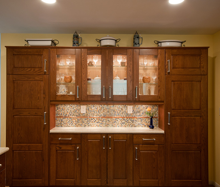 Inspiration for a mid-sized transitional u-shaped medium tone wood floor eat-in kitchen remodel in San Diego with raised-panel cabinets, medium tone wood cabinets, solid surface countertops, an integrated sink, multicolored backsplash, mosaic tile backsplash, stainless steel appliances and a peninsula