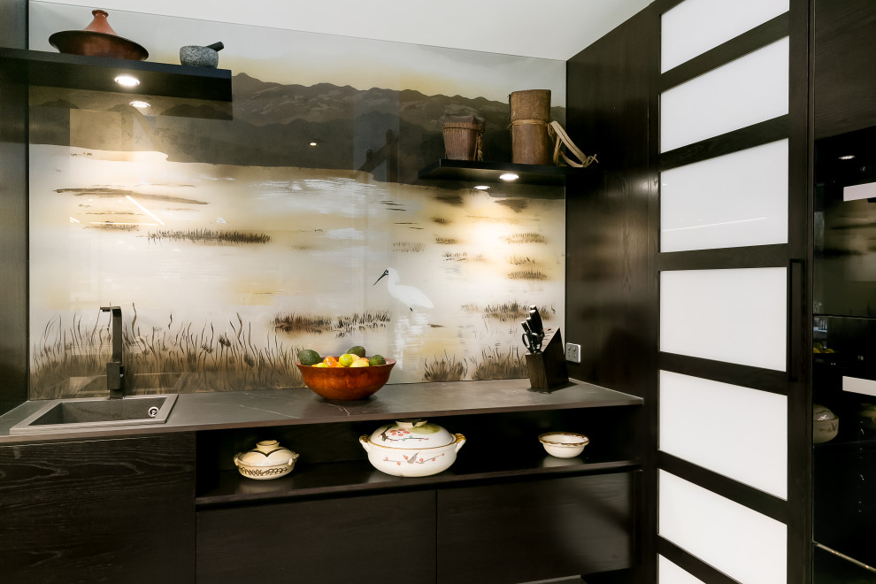 Mid-sized asian l-shaped kitchen pantry in Adelaide with a drop-in sink, dark wood cabinets, solid surface benchtops, multi-coloured splashback, glass sheet splashback, panelled appliances, concrete floors, with island, grey floor and black benchtop.