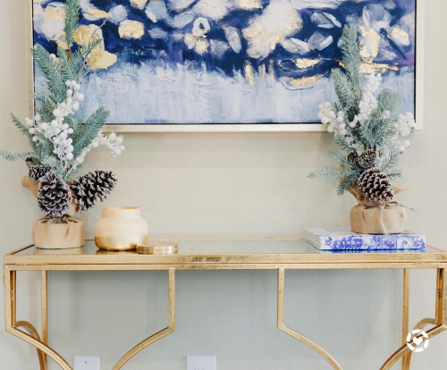 Gold console table decorated with mini snowy pine trees, pinecones, and gold accents for holiday decor inspiration.
