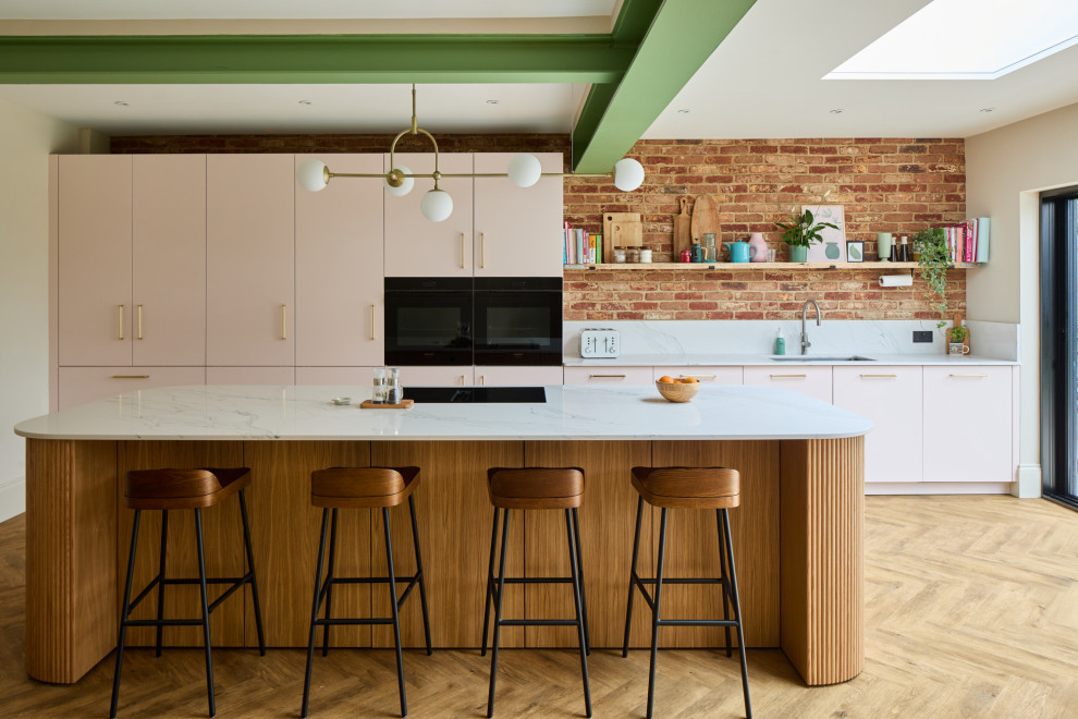 This is an example of a medium sized contemporary single-wall open plan kitchen in London with flat-panel cabinets, pink cabinets, engineered stone countertops, an island and white worktops.
