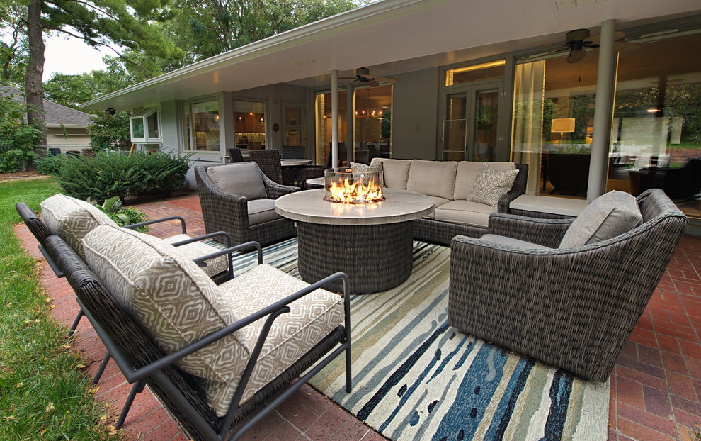 Design ideas for a large midcentury backyard patio in Omaha with a fire feature, brick pavers and a roof extension.