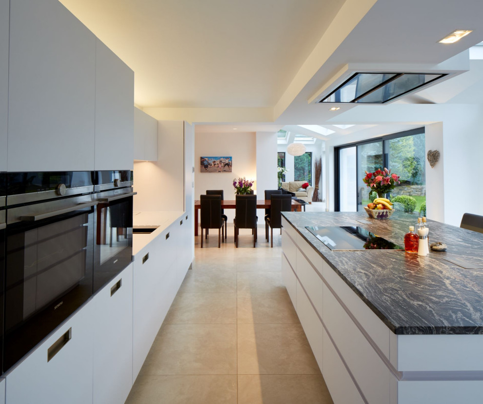 Photo of a mid-sized contemporary single-wall eat-in kitchen in Other with flat-panel cabinets, white cabinets, granite benchtops, metallic splashback, mirror splashback, panelled appliances, with island and blue benchtop.