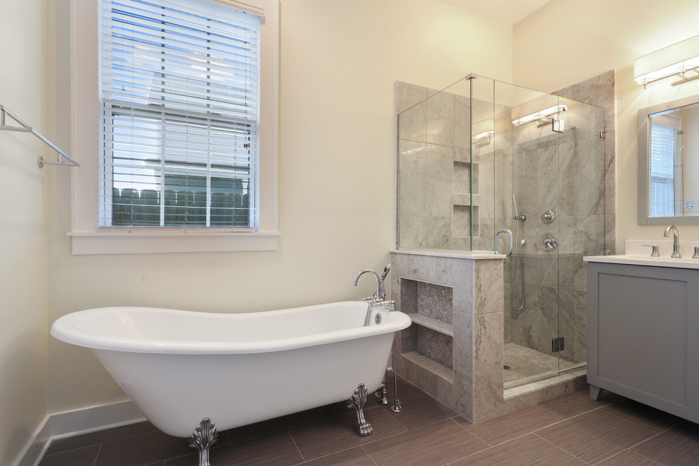 Photo of a mid-sized transitional master bathroom in New Orleans with shaker cabinets, grey cabinets, a claw-foot tub, a corner shower, a two-piece toilet, gray tile, porcelain tile, beige walls, porcelain floors, an undermount sink and marble benchtops.