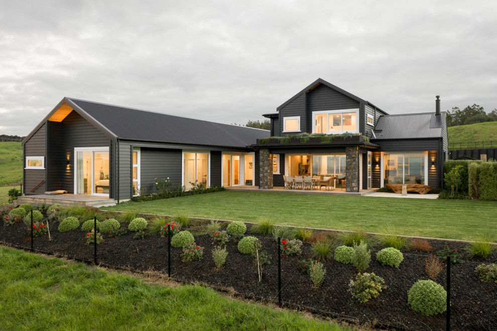 This is an example of a large and black contemporary two floor detached house in Auckland with wood cladding, a pitched roof, a metal roof, a black roof and board and batten cladding.
