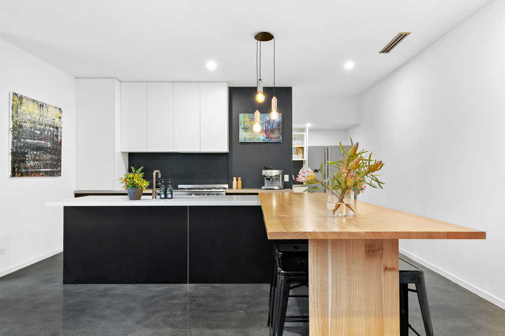 Photo of a mid-sized contemporary galley eat-in kitchen in Geelong with an undermount sink, flat-panel cabinets, quartz benchtops, black splashback, cement tile splashback, stainless steel appliances, concrete floors, with island, grey floor and white benchtop.
