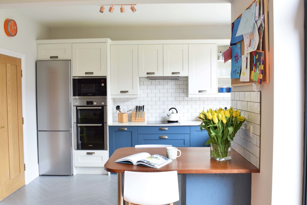Mid-sized contemporary u-shaped eat-in kitchen in Other with a farmhouse sink, shaker cabinets, blue cabinets, recycled glass benchtops, white splashback, ceramic splashback, linoleum floors, a peninsula and grey floor.