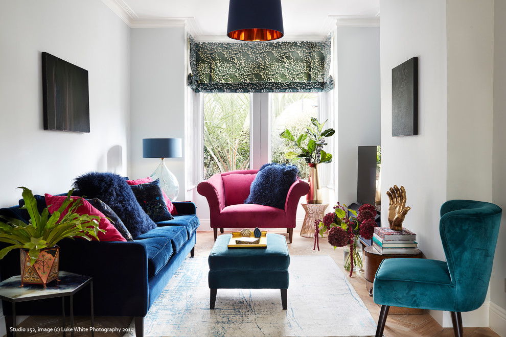 This is an example of a mid-sized eclectic open concept living room in London with blue walls, light hardwood floors, no fireplace and a freestanding tv.