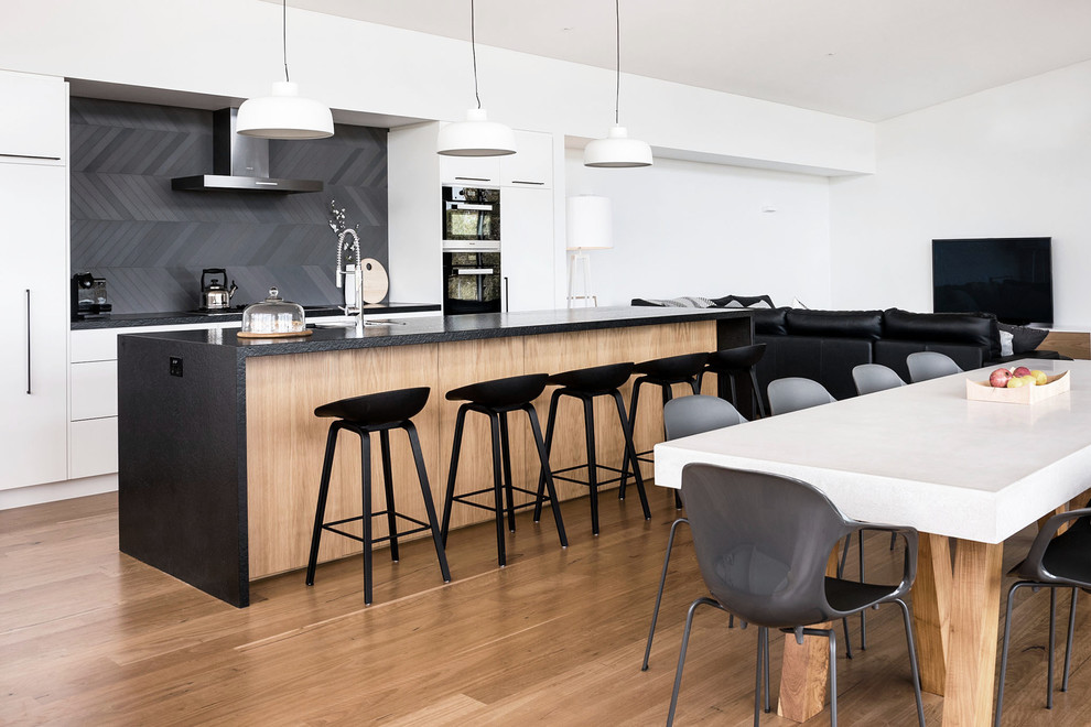 Inspiration for a mid-sized contemporary single-wall eat-in kitchen in Perth with flat-panel cabinets, white cabinets, black appliances, medium hardwood floors, with island, a double-bowl sink, granite benchtops, blue splashback and ceramic splashback.