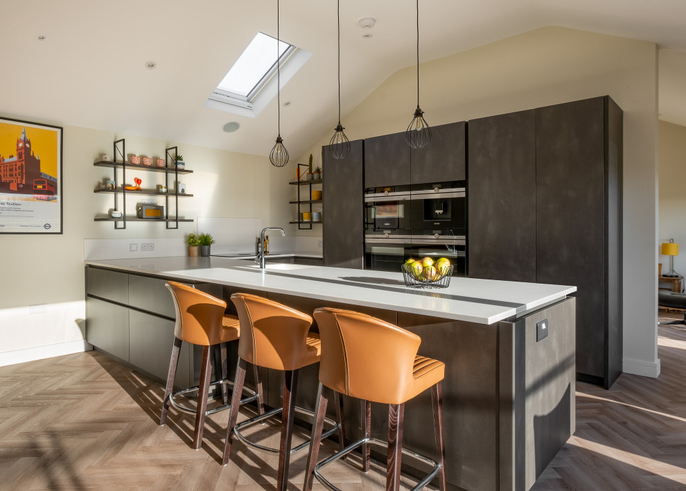Design ideas for a medium sized contemporary galley open plan kitchen in Gloucestershire with an integrated sink, flat-panel cabinets, grey cabinets, composite countertops, grey splashback, black appliances, medium hardwood flooring and grey worktops.