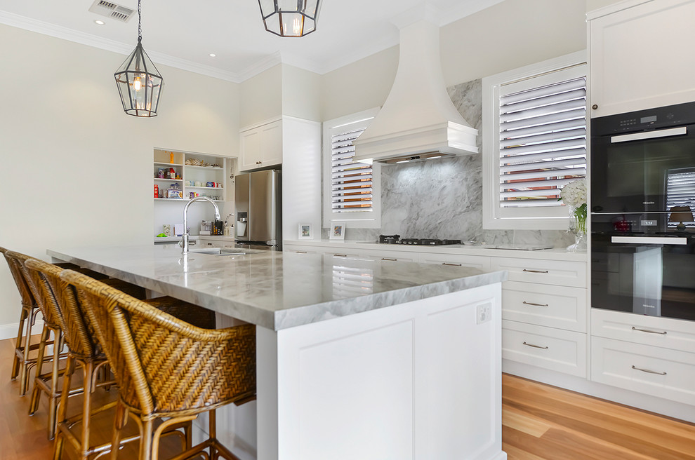 Inspiration for a large contemporary galley open plan kitchen in Sydney with a drop-in sink, shaker cabinets, white cabinets, quartz benchtops, white splashback, marble splashback, stainless steel appliances, light hardwood floors, with island, brown floor and white benchtop.
