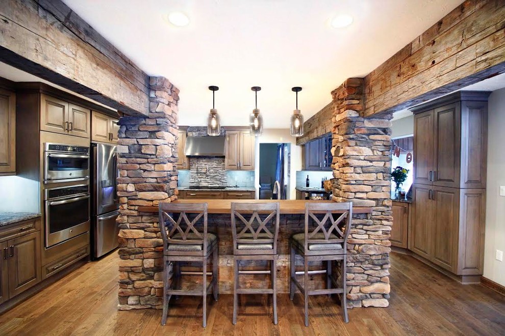 Large mountain style u-shaped medium tone wood floor and brown floor open concept kitchen photo with a single-bowl sink, raised-panel cabinets, gray cabinets, granite countertops, gray backsplash, brick backsplash, stainless steel appliances and an island