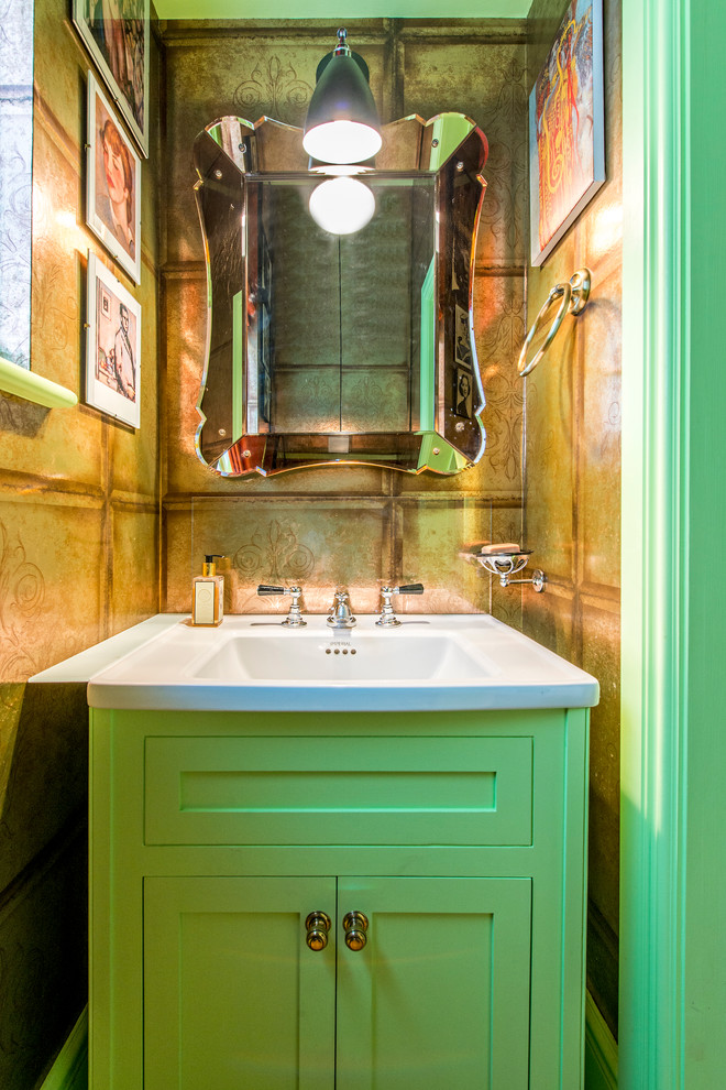 Small eclectic powder room in London with green cabinets and an integrated sink.