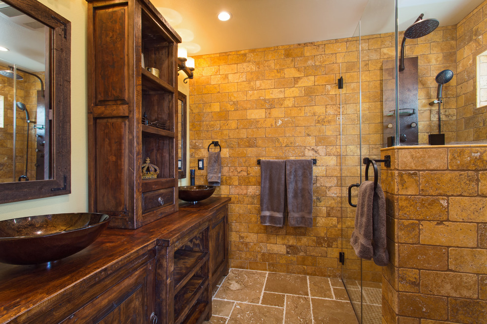 Design ideas for a mid-sized master bathroom in Los Angeles with furniture-like cabinets, distressed cabinets, a curbless shower, a two-piece toilet, yellow tile, travertine, beige walls, travertine floors, a vessel sink, wood benchtops, beige floor and a hinged shower door.