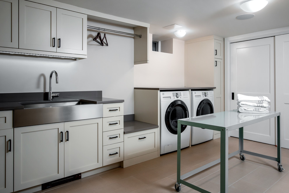 Inspiration for a transitional laundry room in Boston with a farmhouse sink, shaker cabinets, beige cabinets, quartz benchtops, porcelain floors and a side-by-side washer and dryer.