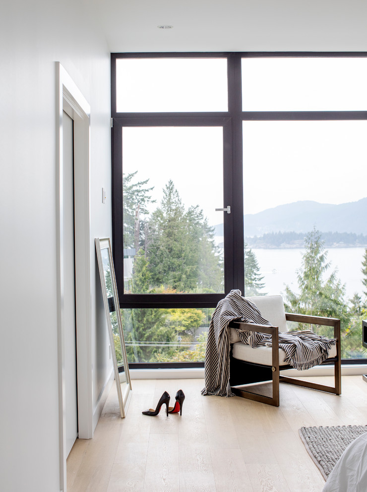 Photo of a large modern master bedroom in Vancouver with white walls, light hardwood floors, a hanging fireplace, a metal fireplace surround and beige floor.