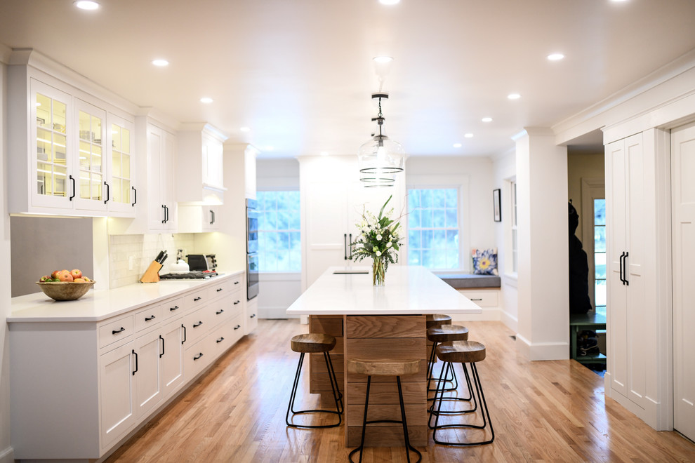 Inspiration for a mid-sized transitional single-wall dark wood floor and brown floor enclosed kitchen remodel in Boston with an undermount sink, shaker cabinets, white cabinets, quartz countertops, stainless steel appliances, an island, white backsplash and subway tile backsplash