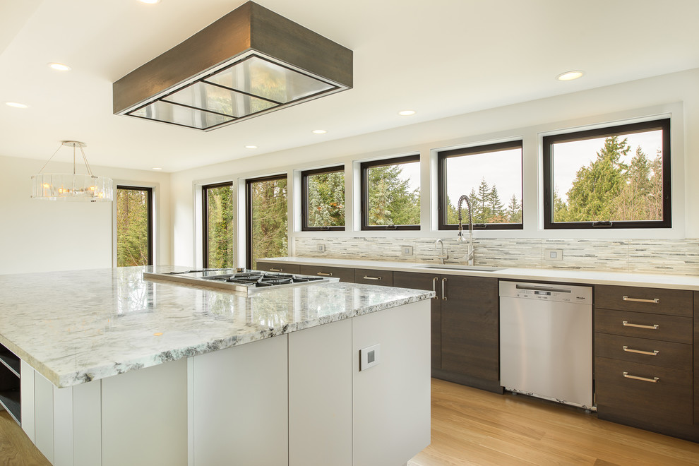 Example of a large transitional u-shaped light wood floor and beige floor open concept kitchen design in Seattle with an undermount sink, flat-panel cabinets, dark wood cabinets, granite countertops, gray backsplash, matchstick tile backsplash, stainless steel appliances, an island and multicolored countertops