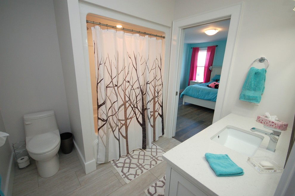 Small transitional porcelain tile and gray floor tub/shower combo photo with white cabinets, a one-piece toilet, white walls, an undermount sink and quartzite countertops