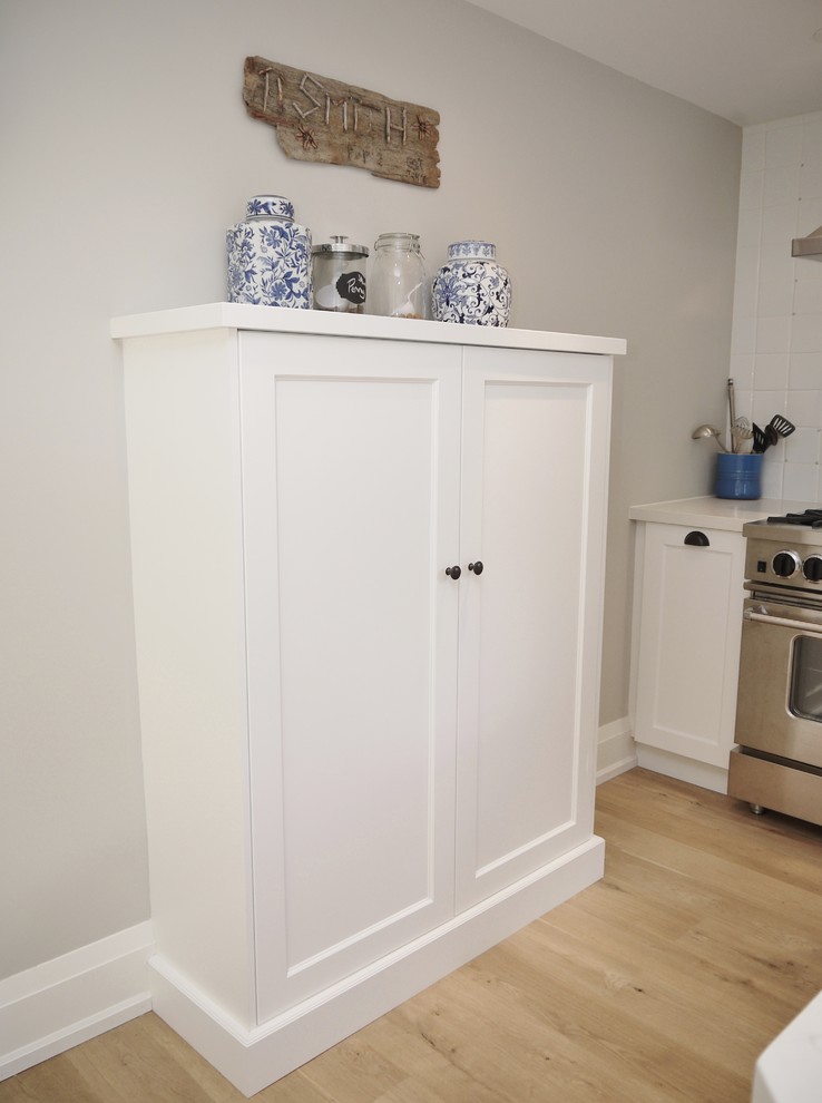 Eat-in kitchen - small transitional l-shaped light wood floor eat-in kitchen idea in Toronto with a farmhouse sink, shaker cabinets, white cabinets, quartz countertops, white backsplash, ceramic backsplash, stainless steel appliances and a peninsula