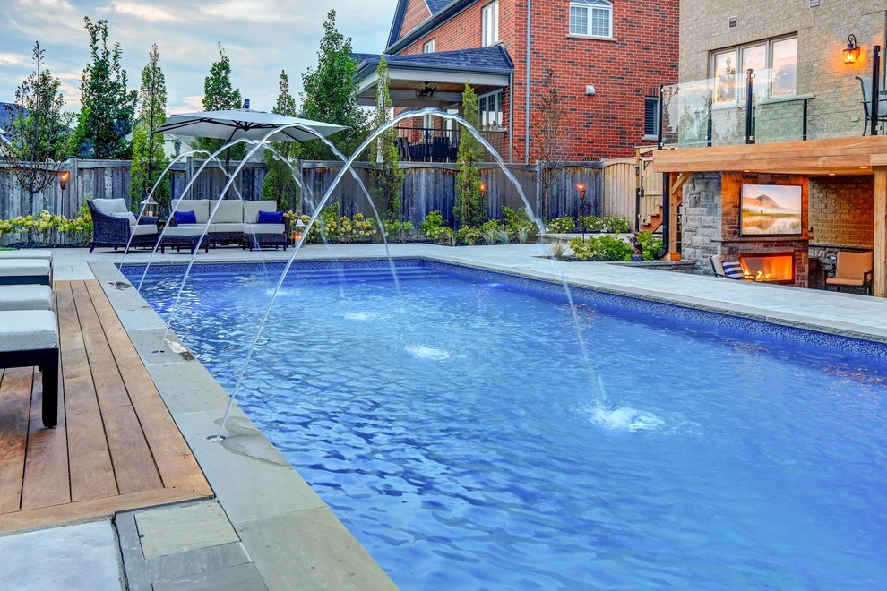 Photo of a mid-sized transitional backyard rectangular pool in Toronto with a pool house and stamped concrete.