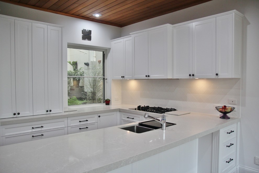 Inspiration for a large traditional u-shaped eat-in kitchen in Melbourne with an undermount sink, recessed-panel cabinets, white cabinets, quartz benchtops, white splashback, ceramic splashback, stainless steel appliances, medium hardwood floors and no island.