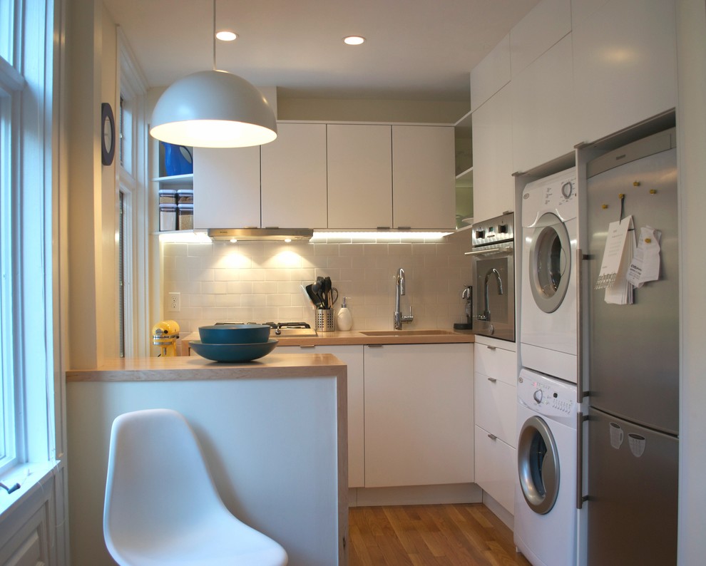 Modern u-shaped eat-in kitchen in Boston with an undermount sink, flat-panel cabinets, white cabinets, wood benchtops, white splashback, subway tile splashback and stainless steel appliances.