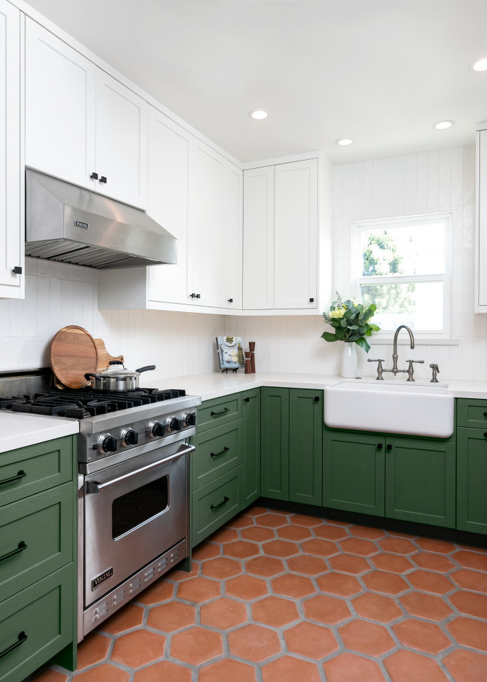 Inspiration for a mid-sized transitional l-shaped separate kitchen in Los Angeles with a farmhouse sink, shaker cabinets, green cabinets, quartz benchtops, white splashback, ceramic splashback, stainless steel appliances, terra-cotta floors, no island, brown floor and white benchtop.