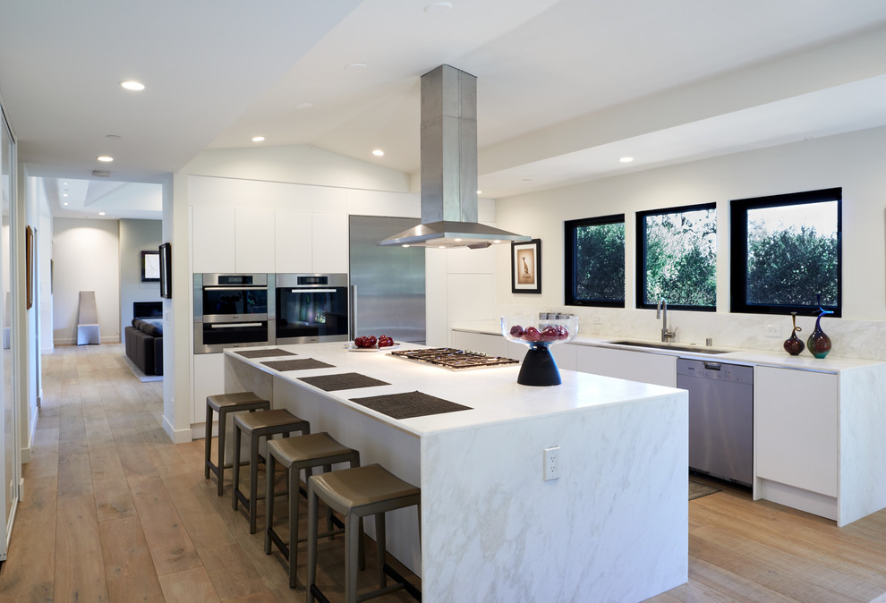 This is an example of a mid-sized contemporary u-shaped eat-in kitchen in San Francisco with flat-panel cabinets, white cabinets, marble benchtops, white splashback, marble splashback, stainless steel appliances, light hardwood floors, with island, white benchtop, an undermount sink and beige floor.
