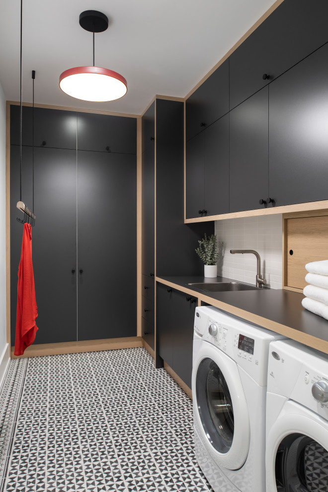 Design ideas for a mid-sized scandinavian l-shaped dedicated laundry room in Toronto with a drop-in sink, flat-panel cabinets, black cabinets, laminate benchtops, white walls, ceramic floors, a side-by-side washer and dryer, black floor and black benchtop.