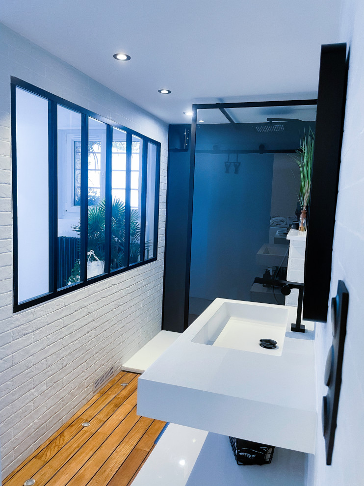Design ideas for an expansive contemporary 3/4 bathroom in Paris with a curbless shower, a wall-mount toilet, white cabinets, white tile, subway tile, white walls, light hardwood floors, a console sink, brown floor, white benchtops, a single vanity, a floating vanity and brick walls.