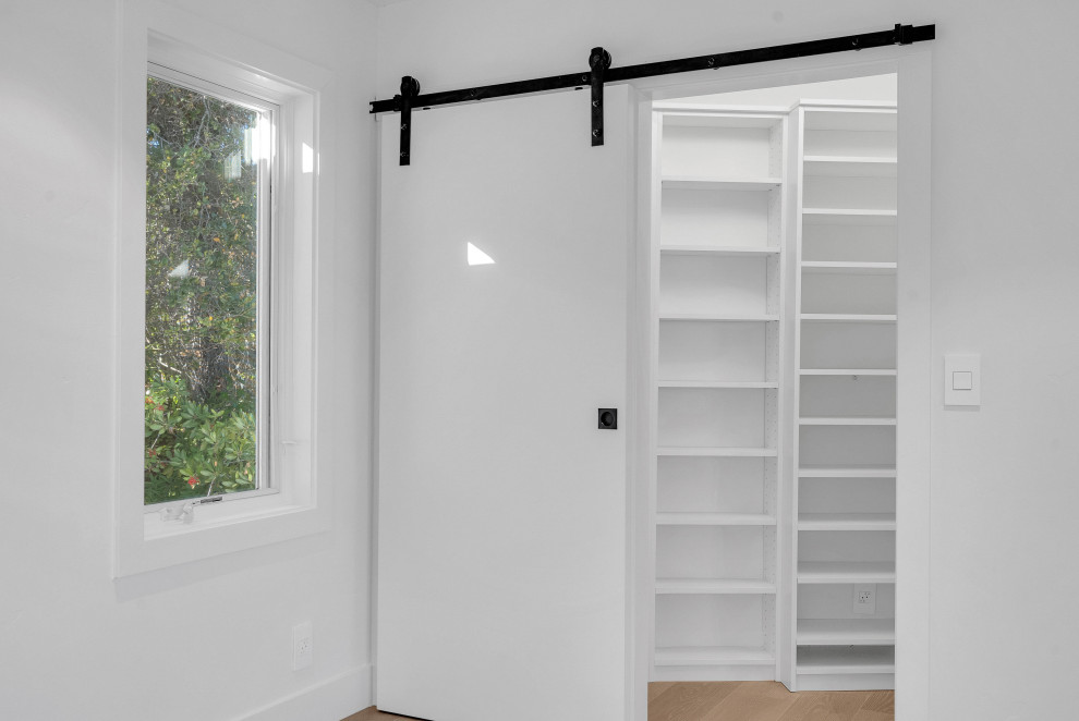 Cette image montre un dressing et rangement minimaliste avec un placard à porte plane, des portes de placard blanches, parquet clair et un sol blanc.
