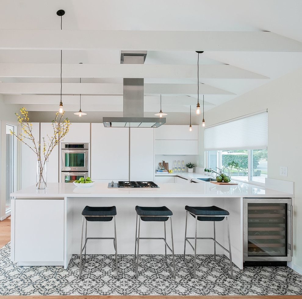 Inspiration for a mid-sized contemporary u-shaped open plan kitchen in San Diego with a single-bowl sink, flat-panel cabinets, white cabinets, quartz benchtops, white splashback, stainless steel appliances, concrete floors and no island.