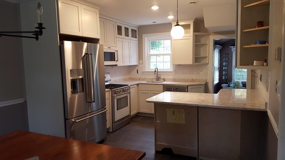 Example of a mid-sized transitional l-shaped porcelain tile and black floor enclosed kitchen design in Baltimore with an undermount sink, shaker cabinets, white cabinets, quartzite countertops, stainless steel appliances, a peninsula and white countertops