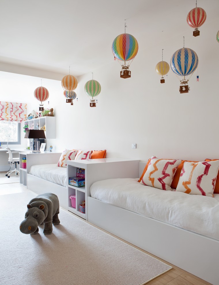 Photo of a large contemporary gender-neutral kids' room in Madrid with white walls and light hardwood floors.
