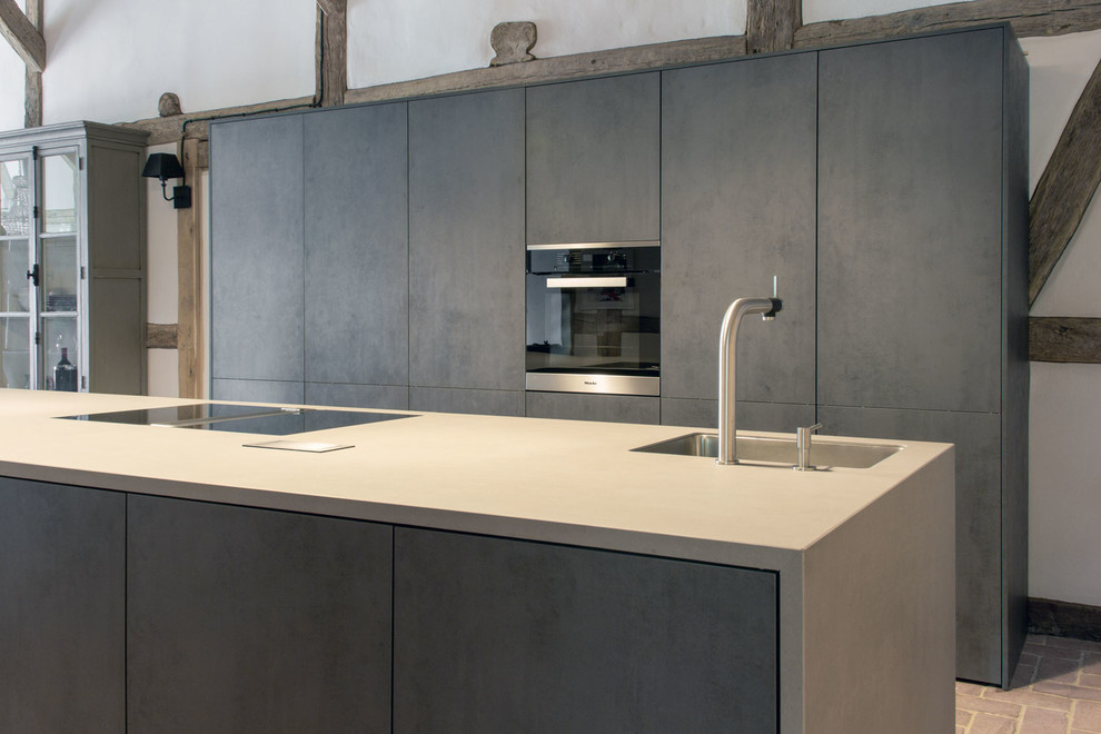 Idee per un'ampia cucina moderna con lavello integrato, ante lisce, ante grigie, top in cemento, elettrodomestici neri e pavimento in mattoni