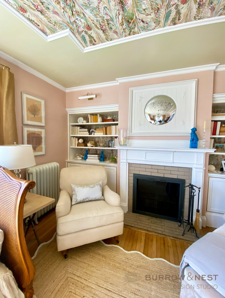 Design ideas for a mid-sized beach style enclosed living room in Providence with a library, pink walls, light hardwood floors, a standard fireplace, a wood fireplace surround, no tv, beige floor, wallpaper and wallpaper.