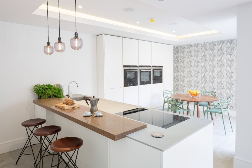 Photo of a small contemporary l-shaped eat-in kitchen in Oxfordshire with a single-bowl sink, white cabinets, marble floors, no island, flat-panel cabinets, concrete benchtops, white splashback, ceramic splashback, white appliances and grey floor.