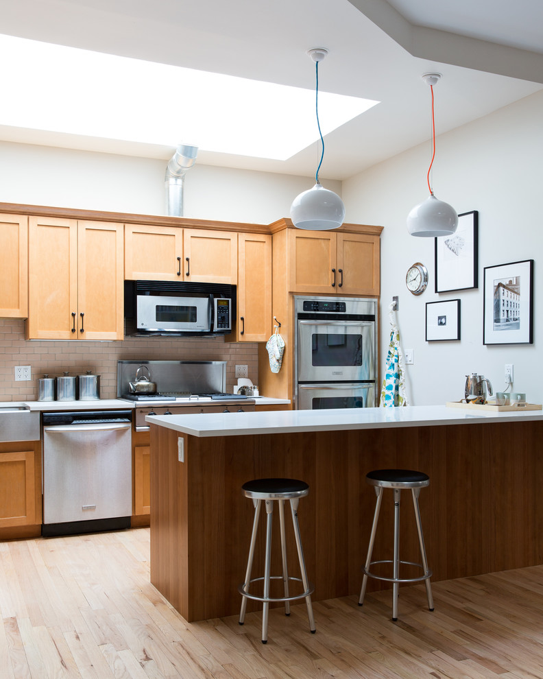 Example of a 1960s light wood floor kitchen design in New York with a farmhouse sink, recessed-panel cabinets, medium tone wood cabinets, quartz countertops, pink backsplash, ceramic backsplash, stainless steel appliances and an island
