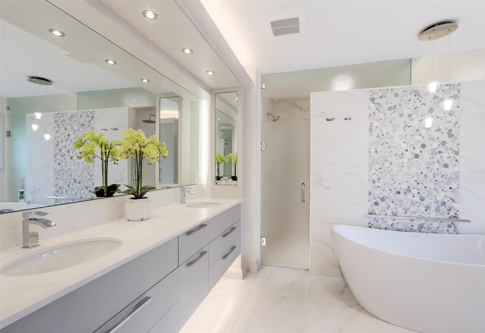 Mid-sized contemporary master bathroom in Toronto with a freestanding tub, white tile, marble, grey walls, marble floors, an undermount sink, engineered quartz benchtops, white benchtops, flat-panel cabinets, grey cabinets and white floor.